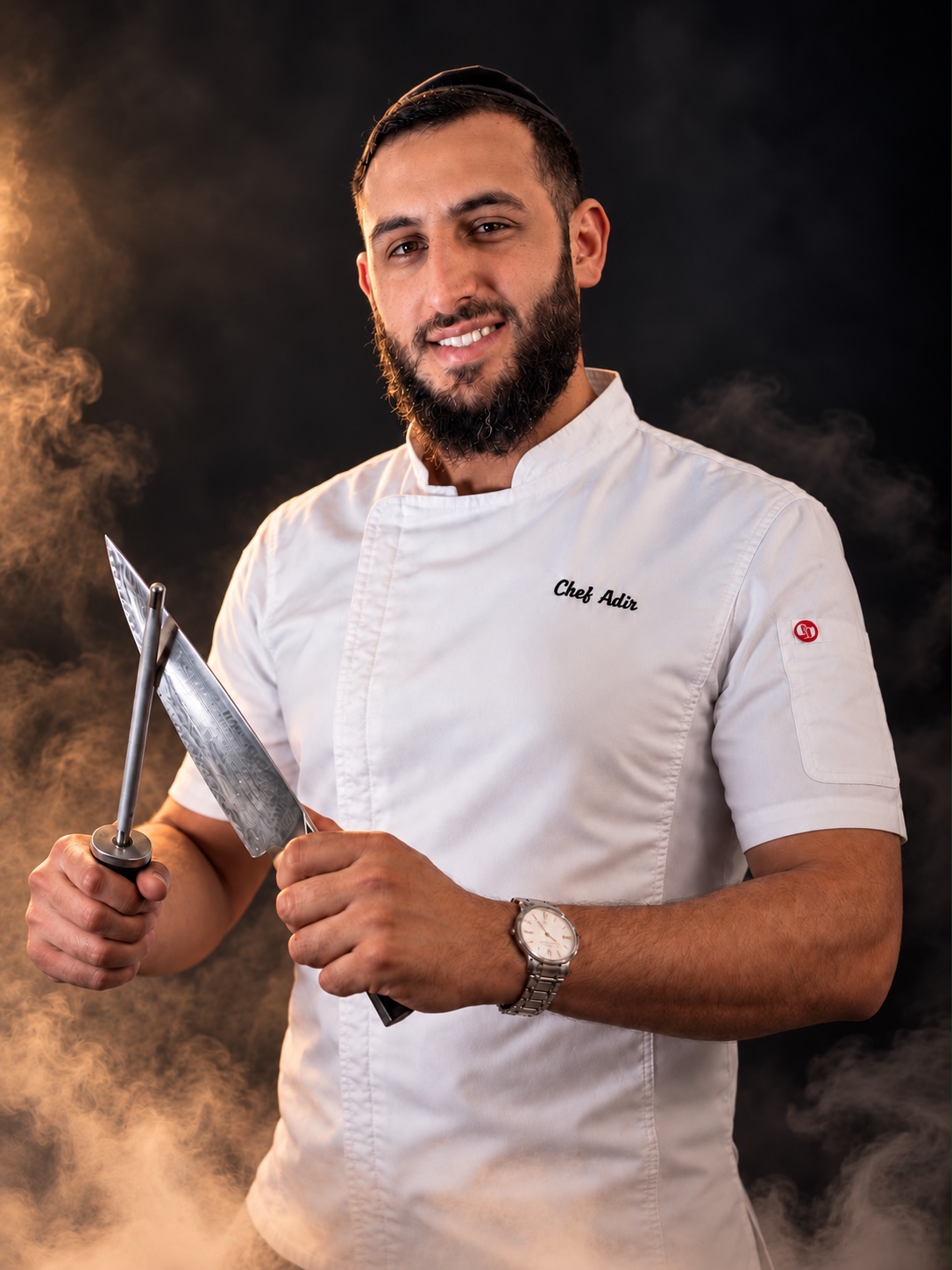 Chef Adir in his chef jacket, holding a chef knife and honing steel